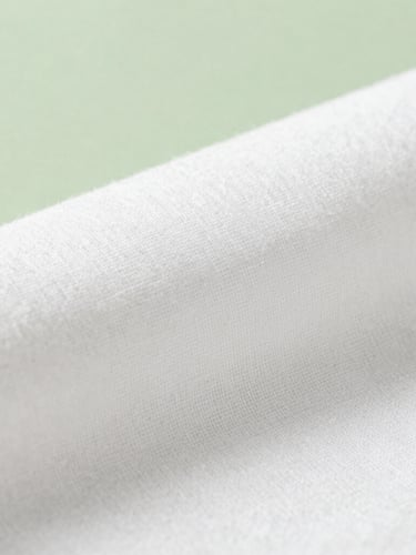 Macro shot of organic white cotton fabric texture, soft natural morning daylight filtering through, calming sage green background accent, minimalist composition