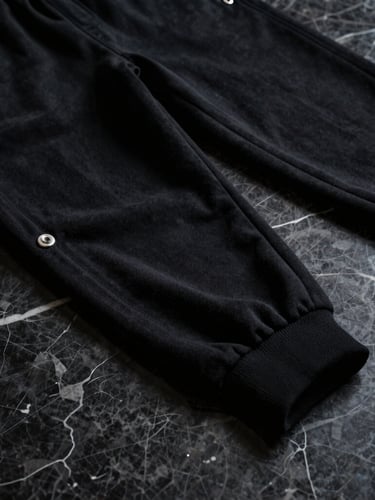 Close-up of structured heavy-gauge black cotton jogger stitching on a dark marble surface, sharp silver hardware details, low-key lighting