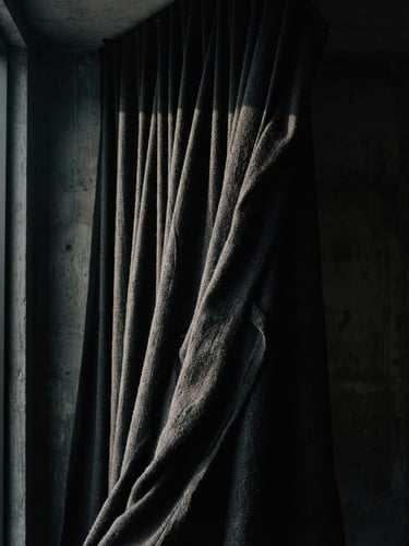 Dark moody editorial photography of a heavy-gauge textile drape inside a minimalist concrete interior, dramatic side-lighting, deep obsidian tones