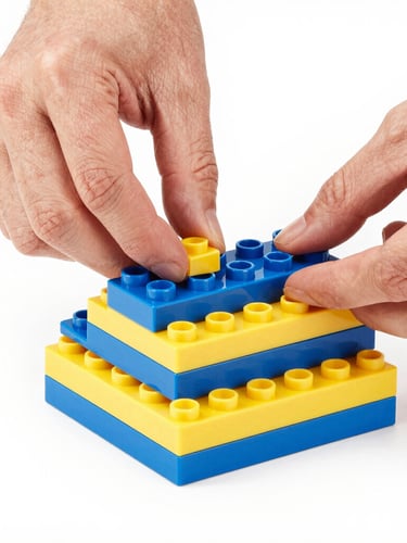 Close-up of hands assembling vibrant blue and yellow building bricks, bright high-key product photography, crisp studio lighting, clean white background, sharp focus, 50mm portrait