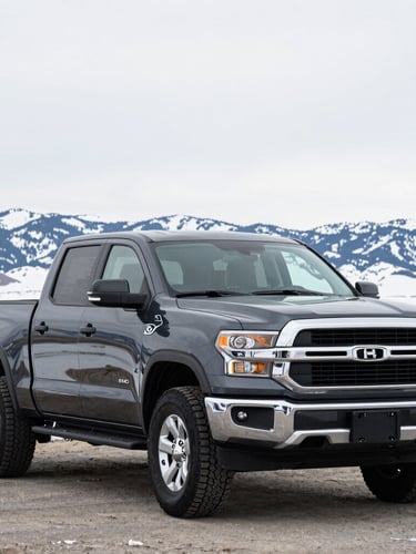 Sharp eye-level shot of a clean, dark-colored pickup truck ready for Idaho winters, parked outdoors on a crisp overcast day with snow-capped mountains in the far distance.