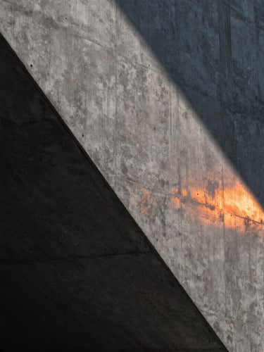 Close-up of a high-end dark architectural concrete wall with sharp linear shadows and a single orange light strip reflecting on the surface, clean minimal composition