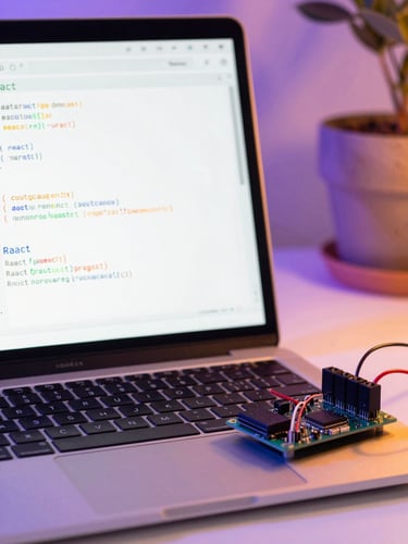 Close-up of a modern laptop screen displaying clean React code, a microcontroller with neatly wired sensors beside it, bright workspace lighting, purple and orange ambient tones.