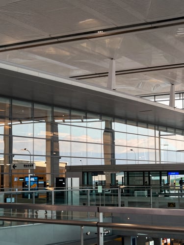 Wide architectural view of a modern airport terminal with soft golden hour light reflecting on glass facades, clean lines, premium editorial feel