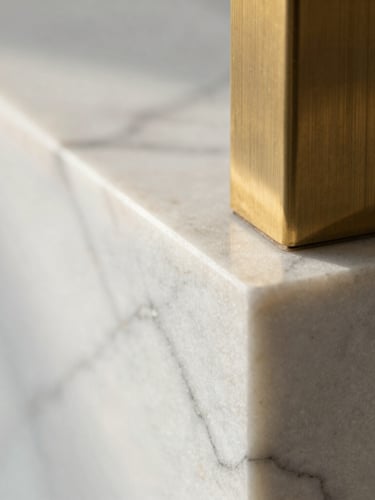 Macro shot of white Carrara marble meeting brushed brass, soft morning light, architectural detail focus.