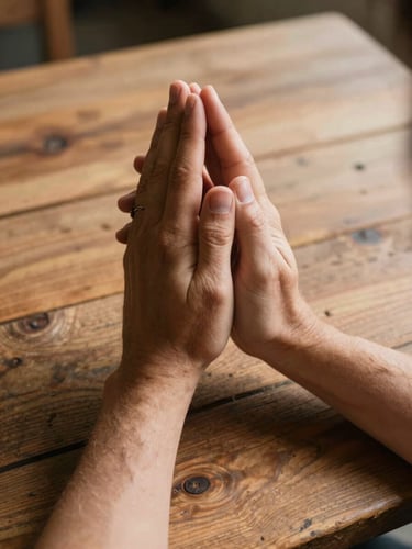 Candid documentary-style close-up of hands joined in prayer over a rustic wooden table, natural warm daylight with high contrast, soft shadows, editorial style.