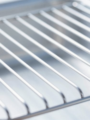 Macro detail shot of a gleaming, professional deep-cleaned oven rack, bright high-key natural daylight, sharp focus