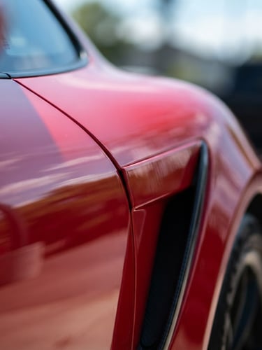Macro close-up of a high-end sports car fender, bright natural daylight highlighting deep glossy paint reflections and sharp metallic curves, shallow depth of field