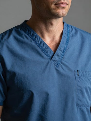 Portrait studio shot of a professional medical scrub made of blue fabric with subtle Faso Dan Fani embroidery details on the collar, high-contrast natural lighting, detailed textile texture.