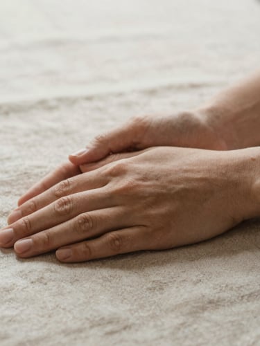 Close-up of hands gently resting on a textured linen surface, soft diffused morning light, shallow depth of field, conveying calm and grounded presence, warm editorial photography, earthy muted tones.