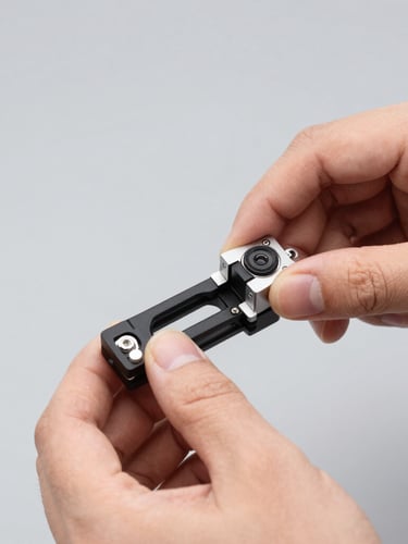 Close-up of hands adjusting a mounting bracket on a clean physical camera hardware, bright utility lighting, sharp focus on hardware details, neutral gray background, 50mm.