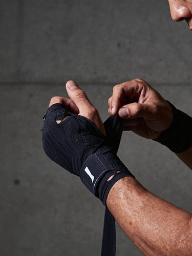 Gritty editorial photography of a focused person tying hand wraps in a high-contrast side-lit concrete studio, sharp focus, 35mm.