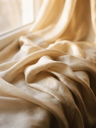 Softly draped beige silk fabric catching warm morning window light, premium editorial fashion photography, 35mm