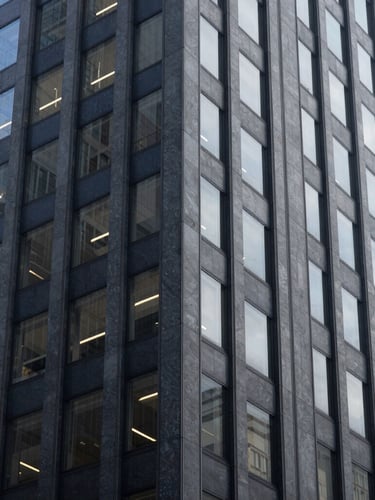 Editorial architectural detail of modern financial district skyscraper in New York, cool natural window light, muted navy and slate tones, shallow depth of field, 35mm