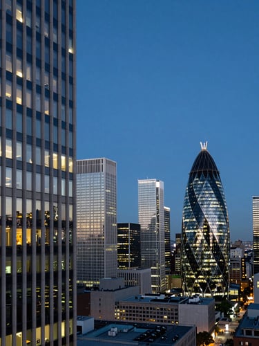 Wide panoramic view of a global financial district at dusk, trading exchange building facade to the left third, deep blue sky overhead, city lights beginning to appear, cool neutral light, no people visible, high contrast architectural geometry