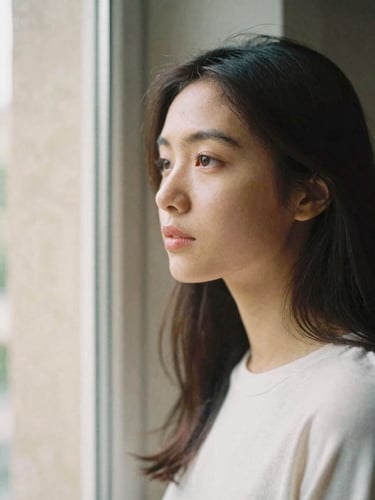 Unposed portrait of Someena looking thoughtfully out of a window, soft natural daylight, warm stone background, shallow depth of field, 35mm film look.