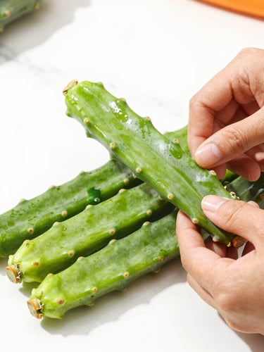 Bright high-key food photography of fresh green nopales being hand-stripped on a clean white marble counter, natural daylight, vibrant green accents, sharp focus.