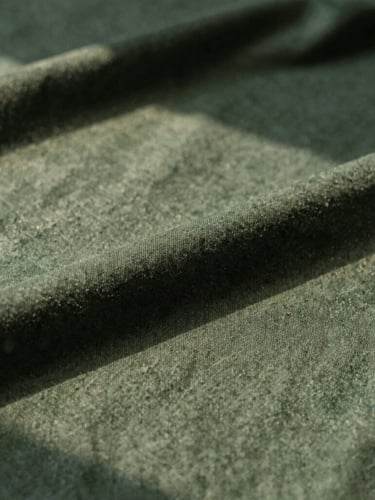 Close-up of premium dark green organic cotton fabric texture under soft warm afternoon sunlight, architectural shadows, editorial style