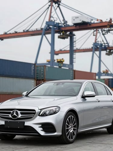 A clean silver Mercedes-Benz luxury sedan staged at a modern shipping dock, container cranes in the background, bright overcast daylight, cool metallic tones, sharp automotive photography, 50mm lens
