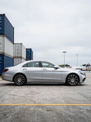 A sharp side-profile shot of a clean Mercedes-Benz S-Class staged on a modern shipping dock at the Miami port, bright overcast daylight.