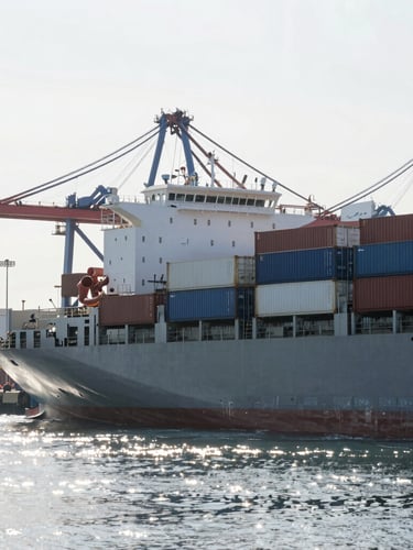 A sleek modern cargo ship loaded with containers at a deep-water port, bright morning light reflecting off the water, sharp automotive transport focus.