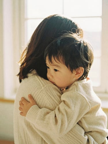 A warm, intimate embrace between a mother and her young child, soft textures of a cream-colored wool sweater, diffused golden-hour light, serene atmosphere, 35mm film.