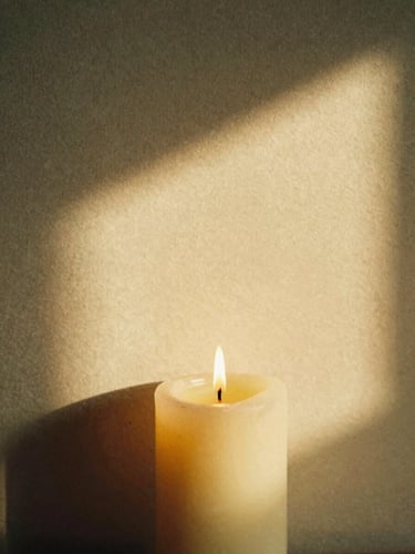 Close-up of a lit candle casting soft shadows on a textured plaster wall, warm golden-hour light, intimate 35mm film grain