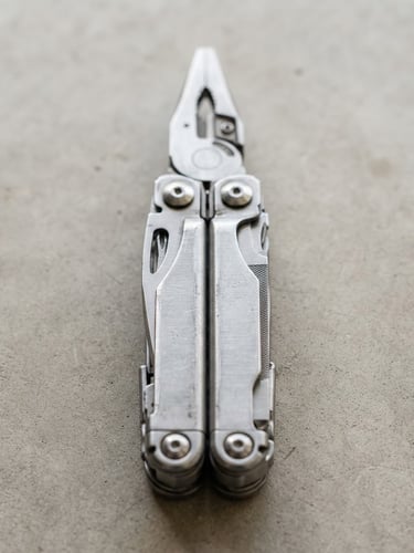 A crisp straight-on portrait shot of a durable steel multi-tool lying on a clean concrete workshop table, bright natural daylight, sharp focus, minimalist studio setting.