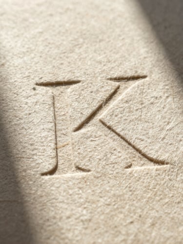 Extreme close-up of textured heavy cotton paper stock with deep letterpress indentation, harsh desert sunlight casting long shadows across the grain.