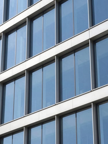Sharp architectural photography of a modern multi-story curtain wall reflecting a bright blue sky, focusing on clean aluminum mullion joints, high contrast daylight, 35mm lens.
