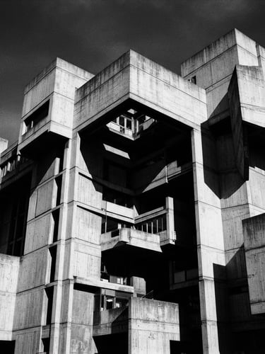 Stark black and white architectural photography of a colossal concrete brutalist building, harsh direct sunlight casting deep geometric shadows, minimalist composition, 35mm film.