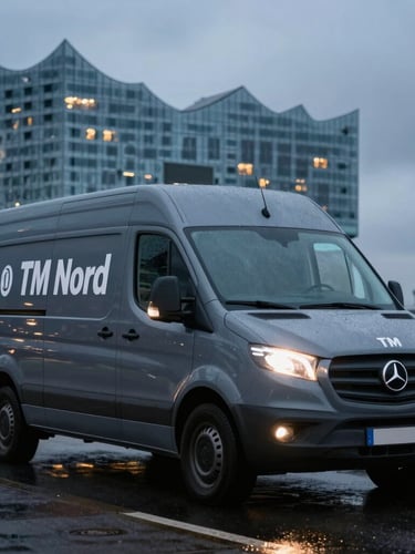 Medium shot of a branded grey service van of TM Nord parked on a wet Hamburg street at dusk, cool streetlights reflecting on the vehicle, with the Elbphilharmonie faintly visible in the background under an overcast sky.