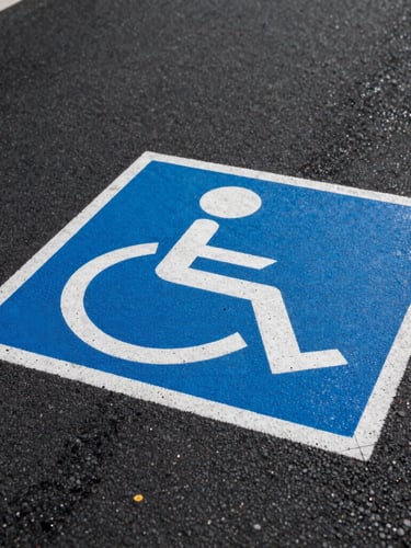 Low-angle perspective shot of a freshly painted blue and white ADA handicap stencil on dark, textured asphalt, crisp wet edges, sharp morning light
