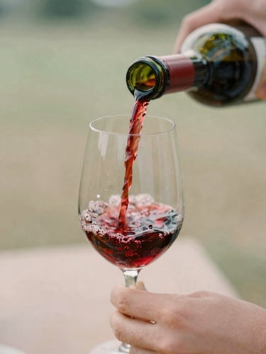 Close-up editorial photograph of hands pouring natural red wine into a delicate glass, soft natural daylight, shallow depth of field, warm tones.