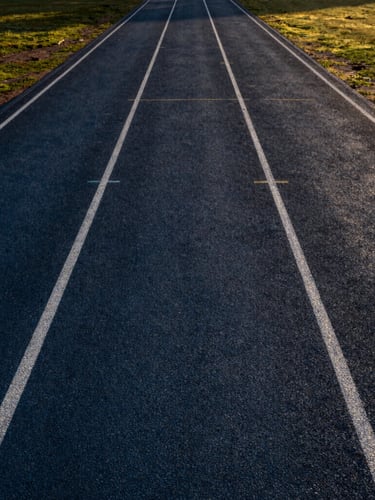 Wide environmental shot of a completed premium athletic track in India, dramatic natural sunlight, high-contrast deep tones, professional sports editorial photography, sharp focus, 35mm lens