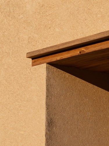 Close-up architectural detail of textured raw plaster walls meeting a heavy oak lintel, warm golden-hour side lighting, tactile textures, 35mm lens.