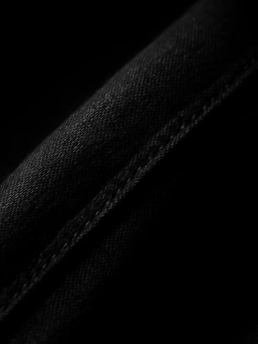 High-contrast studio photography of a heavy matte black fabric seam, deep chiaroscuro shadows, sharp key light highlighting the dense weave, 35mm.