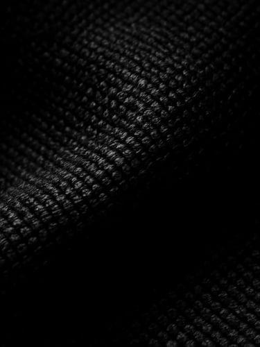 Tight macro crop of heavy black fabric texture, high-contrast chiaroscuro studio lighting, deep shadows, sharp key light highlighting dense weave, 35mm