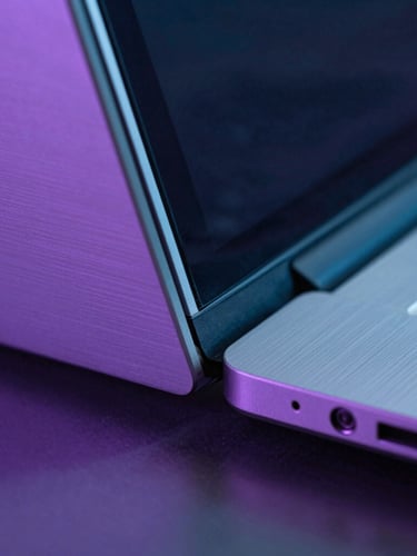 Macro close-up of a premium brushed aluminum laptop hinge and glass screen under moody, low-key violet and cyan ambient backlighting, technical aesthetic.