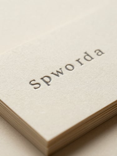 Macro shot of embossed charcoal business cards stacked on warm cream paper, soft side-light highlighting the deep paper texture.