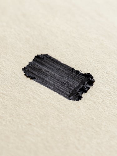 Extreme close-up macro shot of deep black ink pressed onto heavily textured uncoated cream paper stock, soft natural side-light casting subtle paper grain shadows.