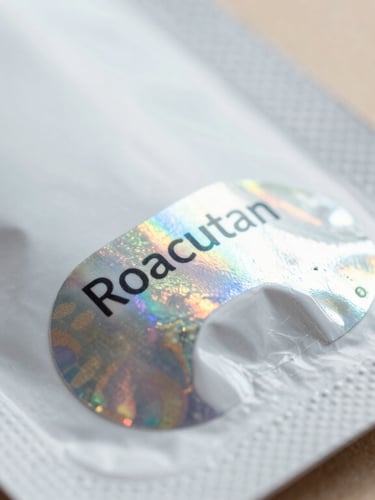 Macro close-up of authentic Roacutan packaging with a holographic security seal, clean clinical daylight, sharp focus on texture