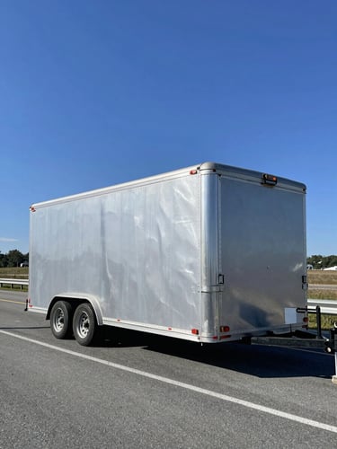 A clean enclosed transport trailer parked on a bright Minnesota highway, polished silver accents, crisp daylight reflection