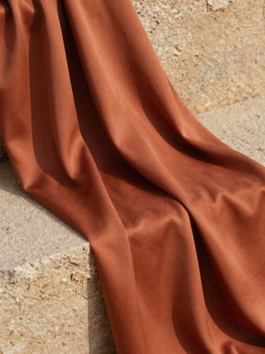 Close-up texture of warm terracotta silk fabric draped over a sand-colored stone, soft natural sunlight, elegant editorial composition
