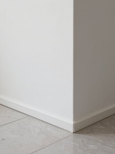 Close-up daylight shot of interior finish detail in a completed home — smooth white wall meeting a polished porcelain floor tile, clean grout lines, sharp corner junction, no people, crisp even light