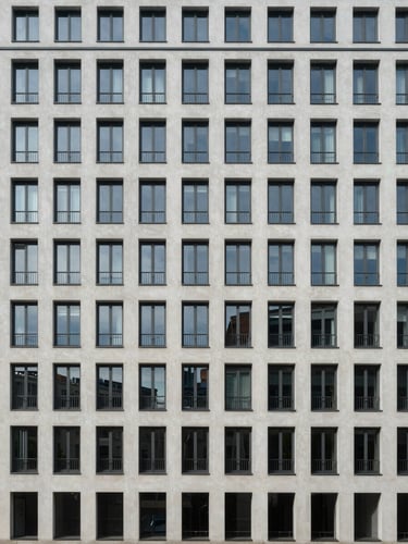 Wide panoramic view of a modernist Berlin residential building facade, photographed straight-on from the street level, symmetrical grid of windows under flat neutral daylight, no people, clinical architectural framing with generous negative space on the left side