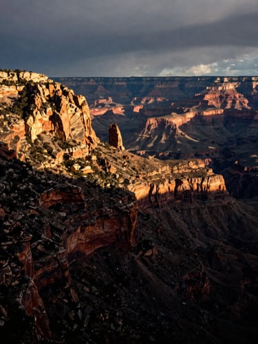 Dramatic vertical portrait of a rugged mountain ridge meeting a deep canyon under moody overcast skies, high contrast, 35mm photography