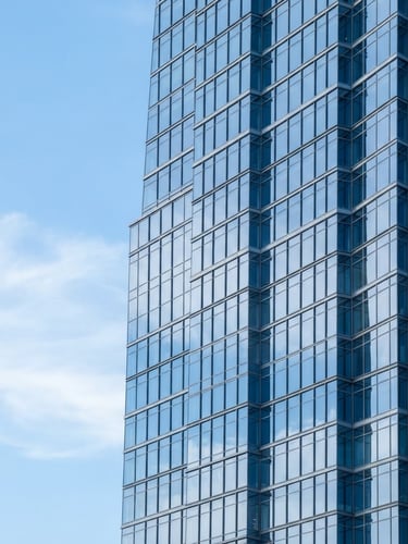 Bright corporate photography of clean modern skyscraper glass facade reflecting blue sky, soft diffused daylight, cool blue tones, 50mm, negative space on the left