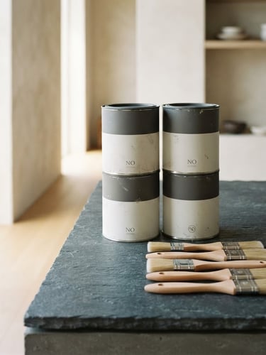 Neat stack of premium paint cans and clean professional brushes on a slate gray surface, bright natural daylight, architectural photography, sharp focus