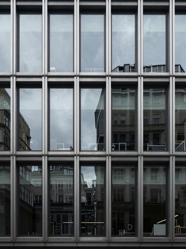 Cool architectural photography of a minimalist London office facade, sharp window reflections, desaturated steel tones, 35mm